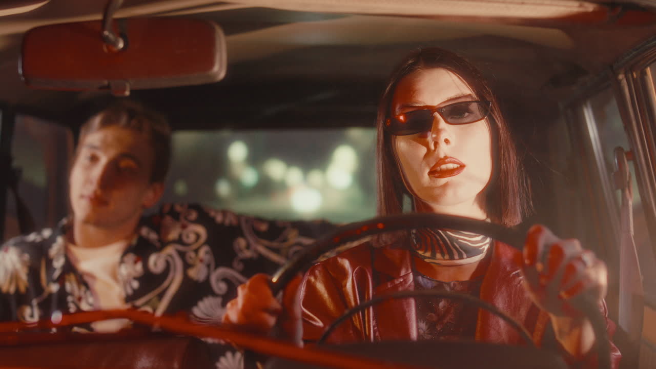 Woman Singing and Driving Vintage Car at Night with Passenger in Back Seat