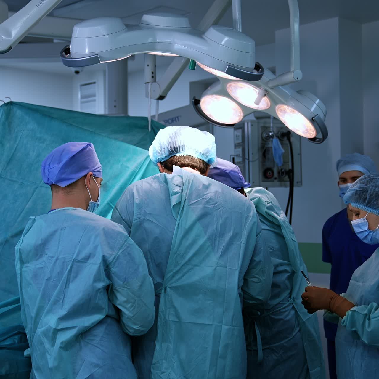 Big group of medics working hard at operation. Doctors standing close to each other over the patient, their backs to camera