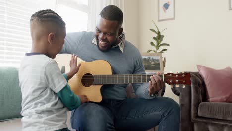 Feliz-Padre-E-Hijo-Afroamericanos-Sentados-En-El-Sofá-Y-Tocando-La-Guitarra,-En-Cámara-Lenta