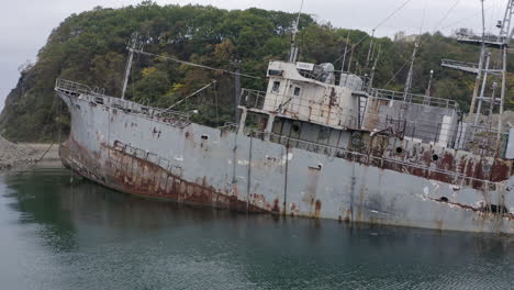 rusty grey half submerged shipwreck anchored near the shore on a cloudy overcast day