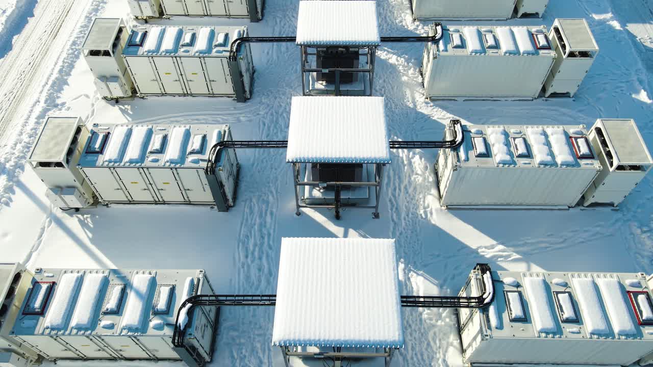 Hovering aerial tilt over large scale 100MW battery storage containers revealing electrical systems and grid infrastructure in harsh winter climate