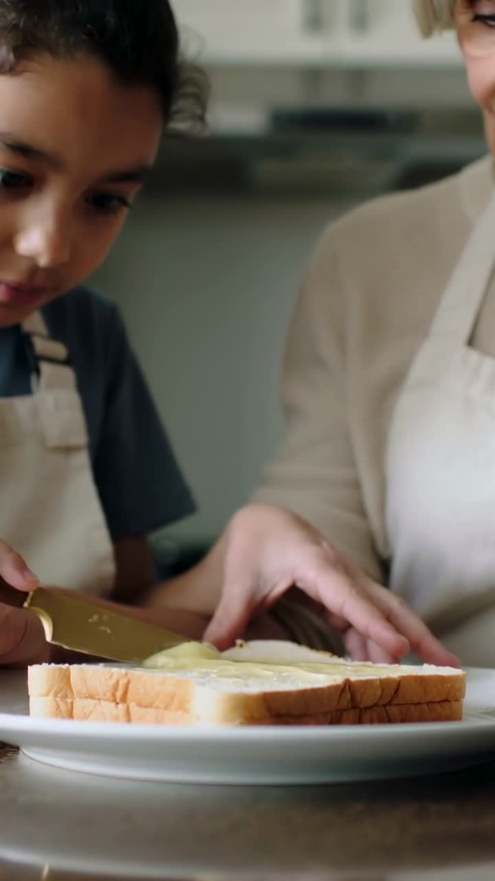 Vertical video: Scooping spread gran teaching child spreading on bread in kitchen gold knife aprons