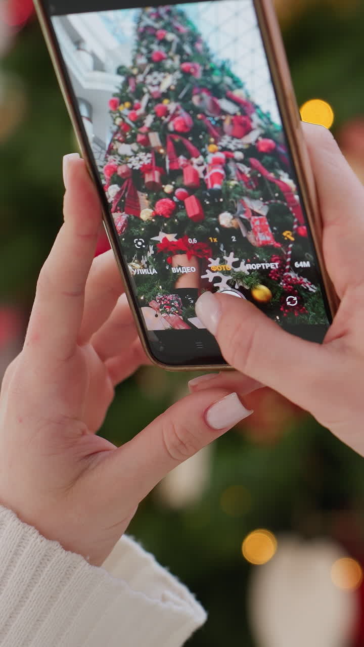 Close-up of woman taking picture of beautifully decorated Christmas tree with smartphone, bright lights and festive ornaments create a joyful holiday atmosphere