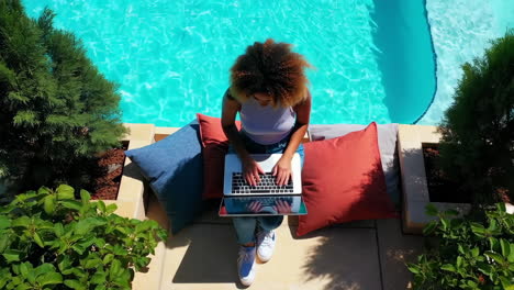 woman working on laptop by a swimming pool