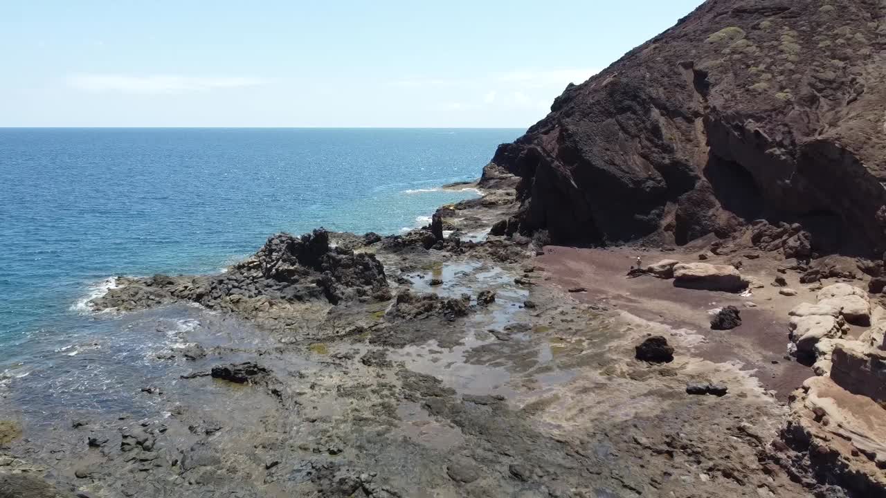Drone flight by the sea over a dark black lava rock landscape in tenerife (canary islands, spain)