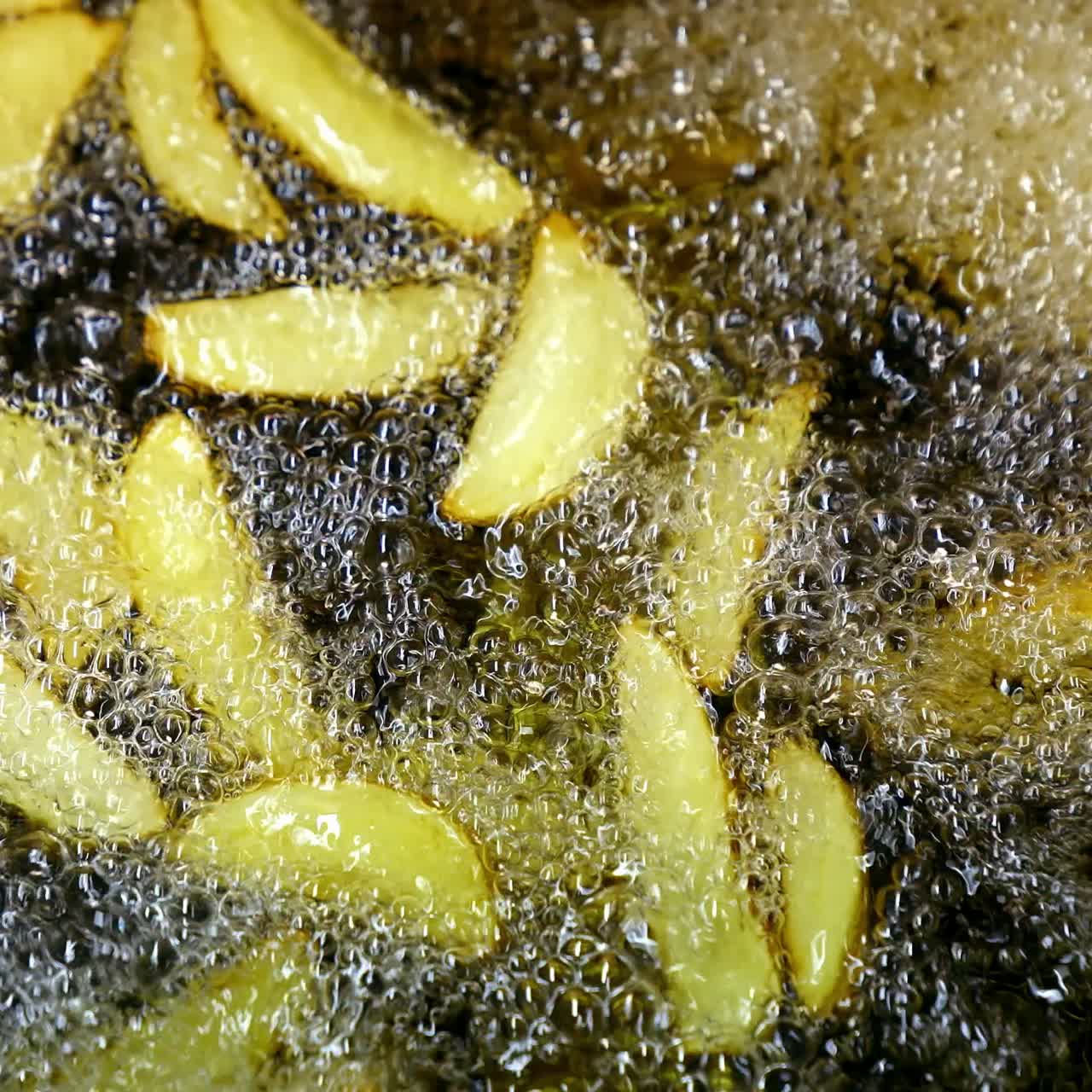 Crispy potato in boiling oil. Bubbles of hot oil during cooking french fries in deep fryer. Process of cooking golden fried potatoes. Macro shot