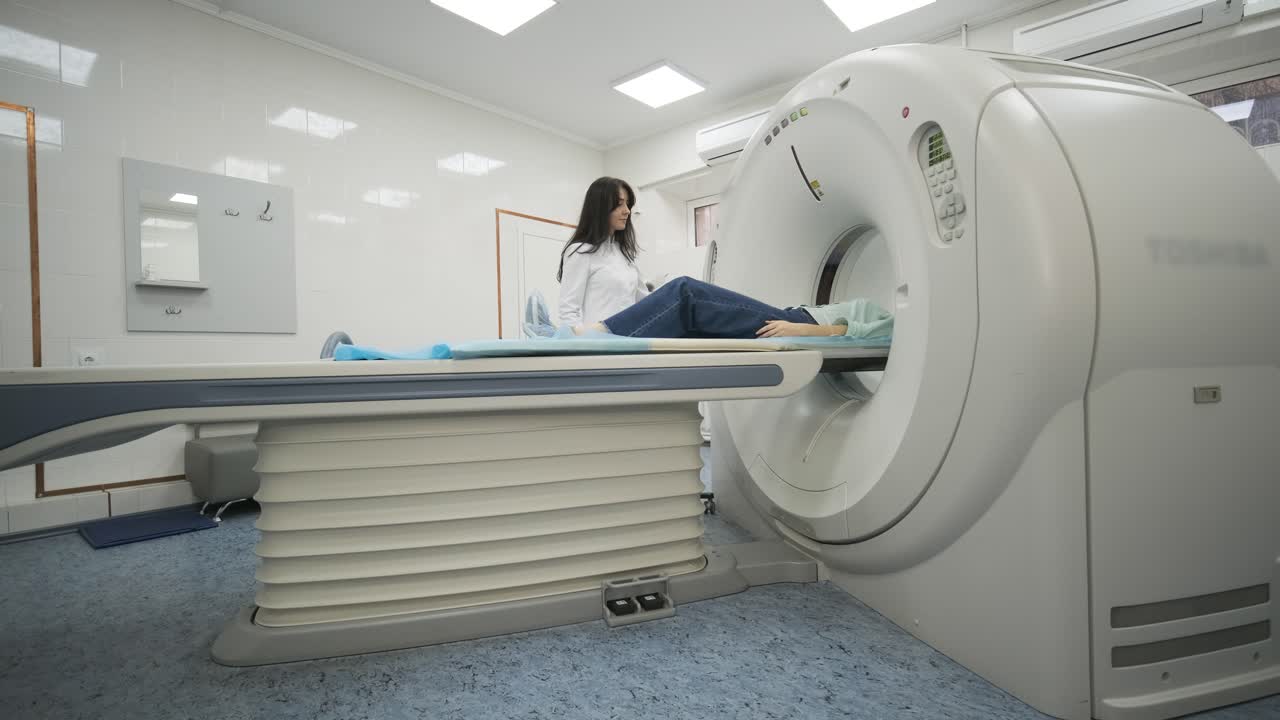 la paciente está siendo sometida a una tomografía computarizada o resonancia magnética bajo la supervisión de un radiólogo en una clínica médica moderna. la paciente está acostada en una cama de tomografía computorizada o mri, moviéndose fuera de la máquina.