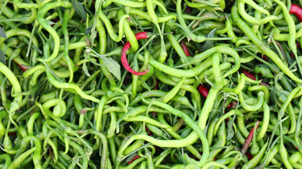 Hromada čerstvých zelených a červených chilli papriček na trhu.