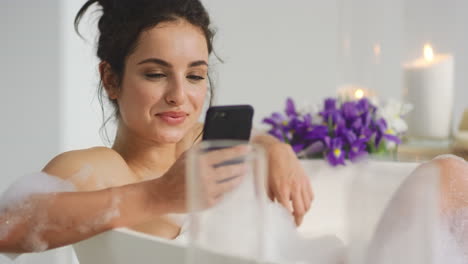 relaxed woman sitting in bath with smartphone