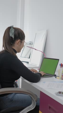 woman typing on a laptop with a green screen at a desk