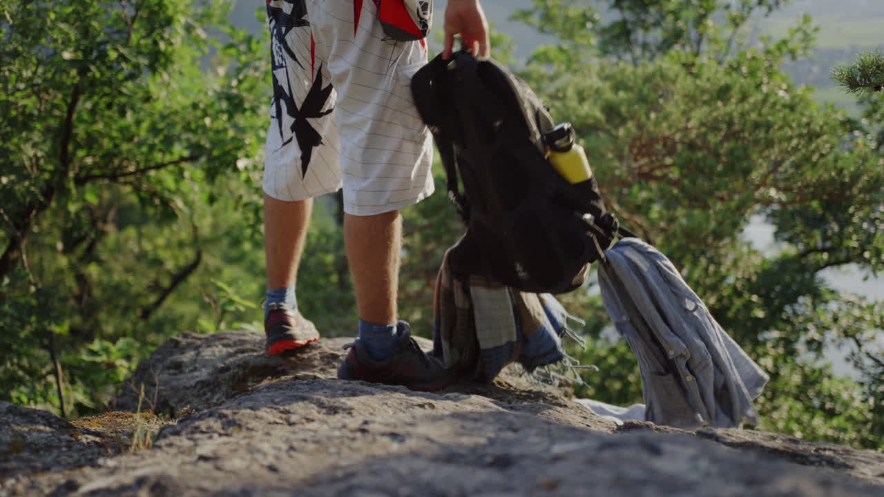 hombre parado, zapatos de senderismo, trekking de montañero de ancho medio, cámara lenta, dejando el equipo de escalada de montañismo, toma de slomo cinematográfica, naturaleza al aire libre, colina rocosa, árboles se rompen