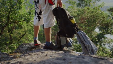 man standing still, hiking trail shoes, medium wide mountaineer trekking, slow motion, putting down mountaineering climbing gear equipment, cinematic slomo shot, outdoor nature, rocky hill trees break