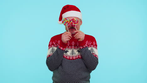 hombre gracioso en suéter de navidad rojo sosteniendo caramelos rayados piruletas escondiéndose detrás de ellos tonto