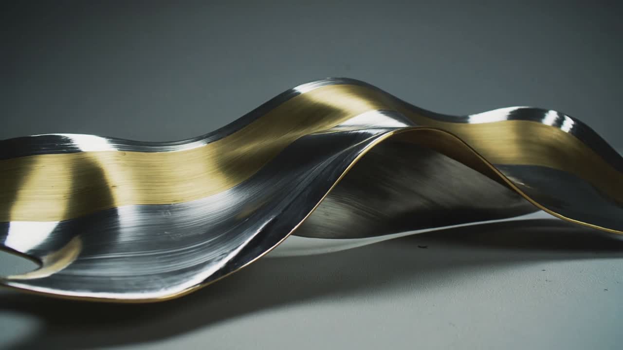 Vertical video: Gold-silver ribbon resting low on desk, frames driving wave, shifting for design