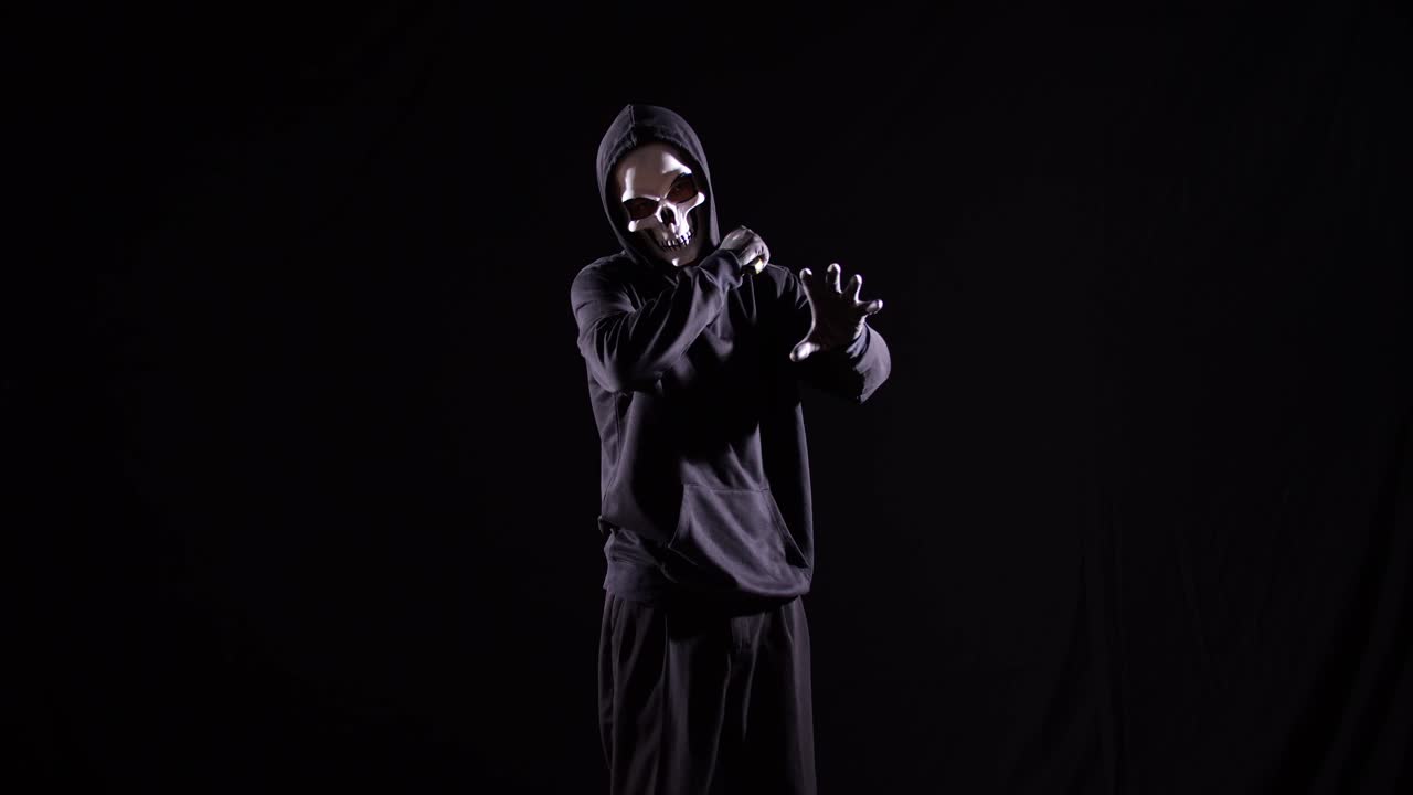 страшный человек в капюшоне с капюшоном, носящий маску хэллоуина, держащий нож и делающий жест, который хочет убить кого-то сумасшедшего на черном фоне