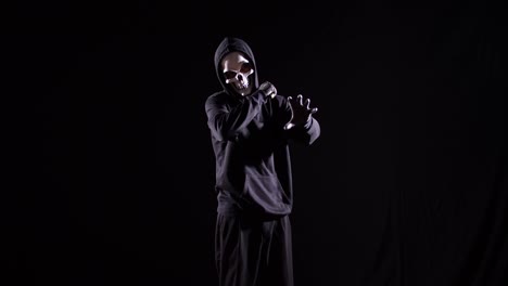 hombre aterrador en la sudadera con capucha usando máscara de halloween sosteniendo un cuchillo y haciendo gestos quieren matar a alguien loco en el fondo negro