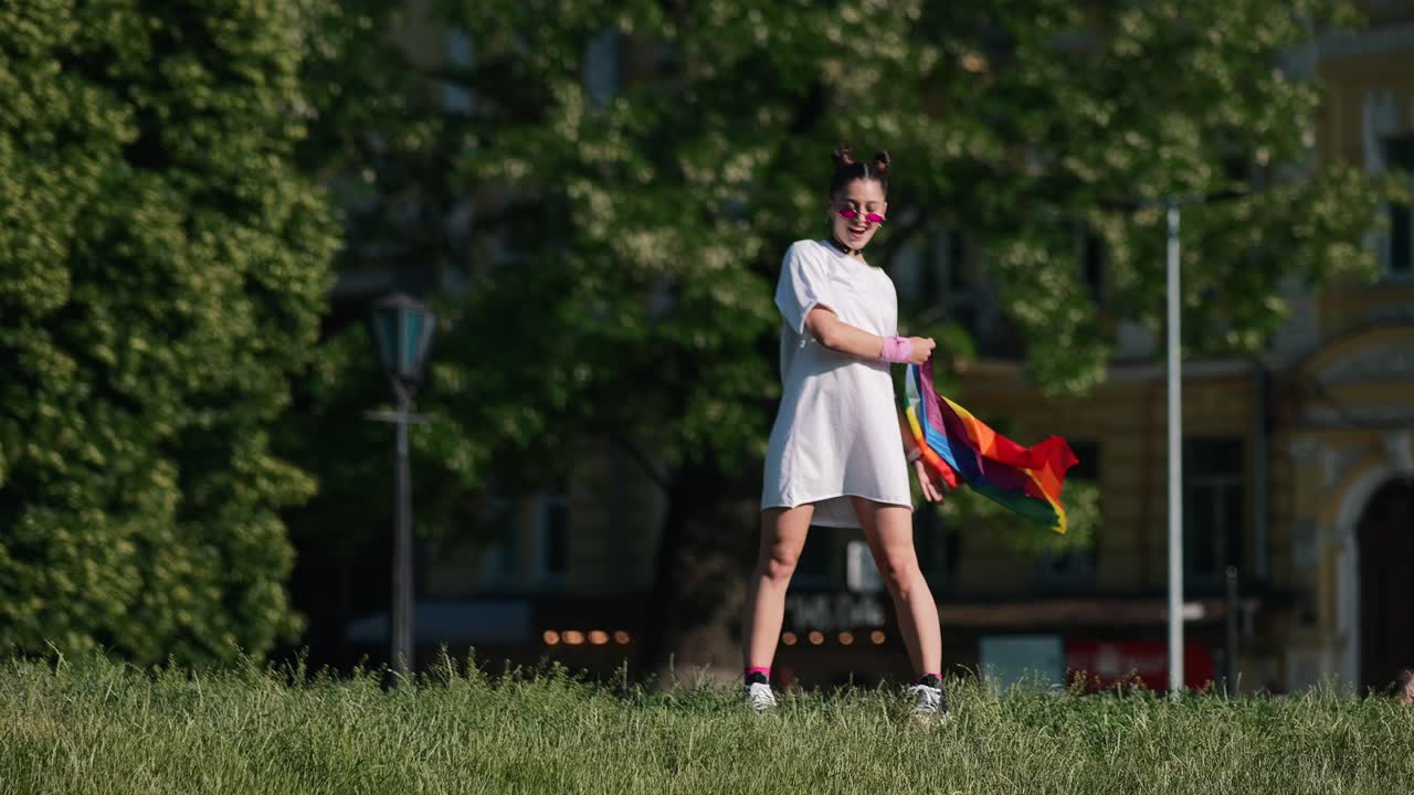 mujer sosteniendo una bandera arco iris en un parque de la ciudad