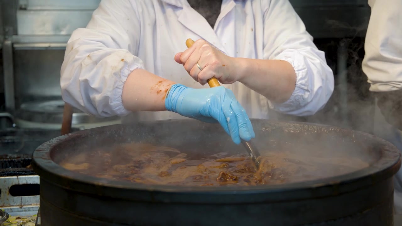 Chef che mescola una grande pentola di stufato sobbollente in una cucina professionale.
