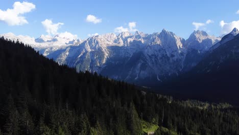 4k drone shot of a forest full of pine trees with the outstanding mountains and rock formations in the background in the beautiful area of the dolomites in north italy