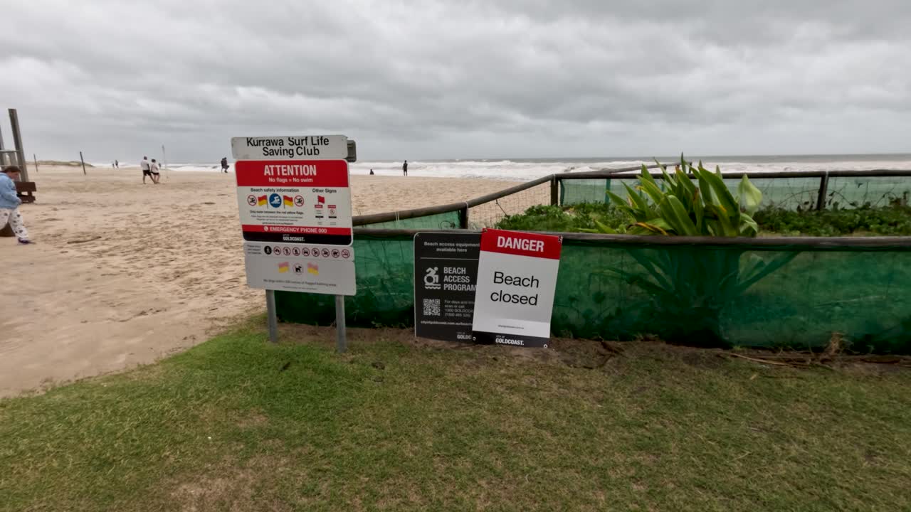사이클론으로 인해 해변이 경고 표지판으로 폐쇄되어 구름이 쌓인 하늘 아래 안전과 환경 문제를 강조합니다.