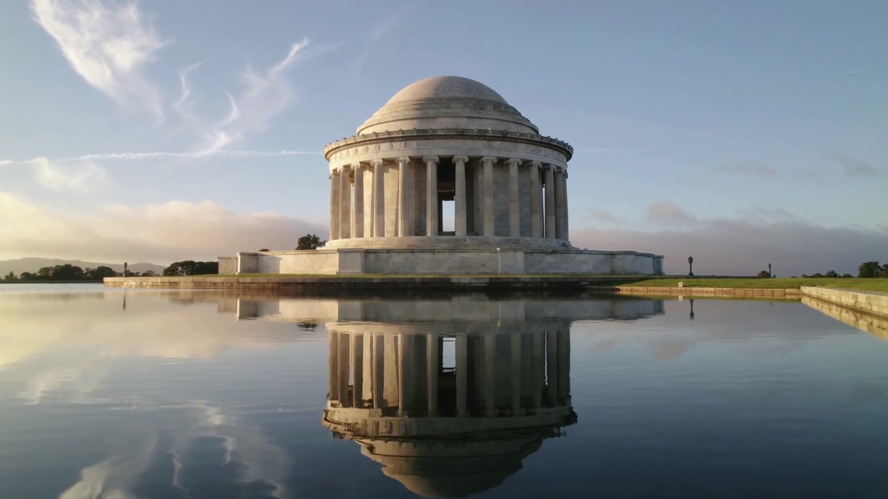 Memoriale neoclassico a cupola che si riflette e cambia con le nuvole di passaggio e i passanti presso una vasca riflettente