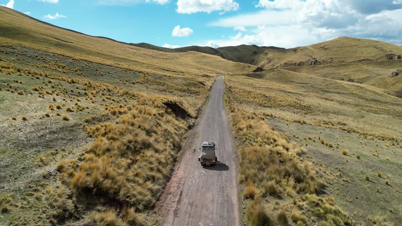 Cinematic aerial shot of a tuk tuk weaving through wild Andean grasslands, golden-green textures glowing under morning light
