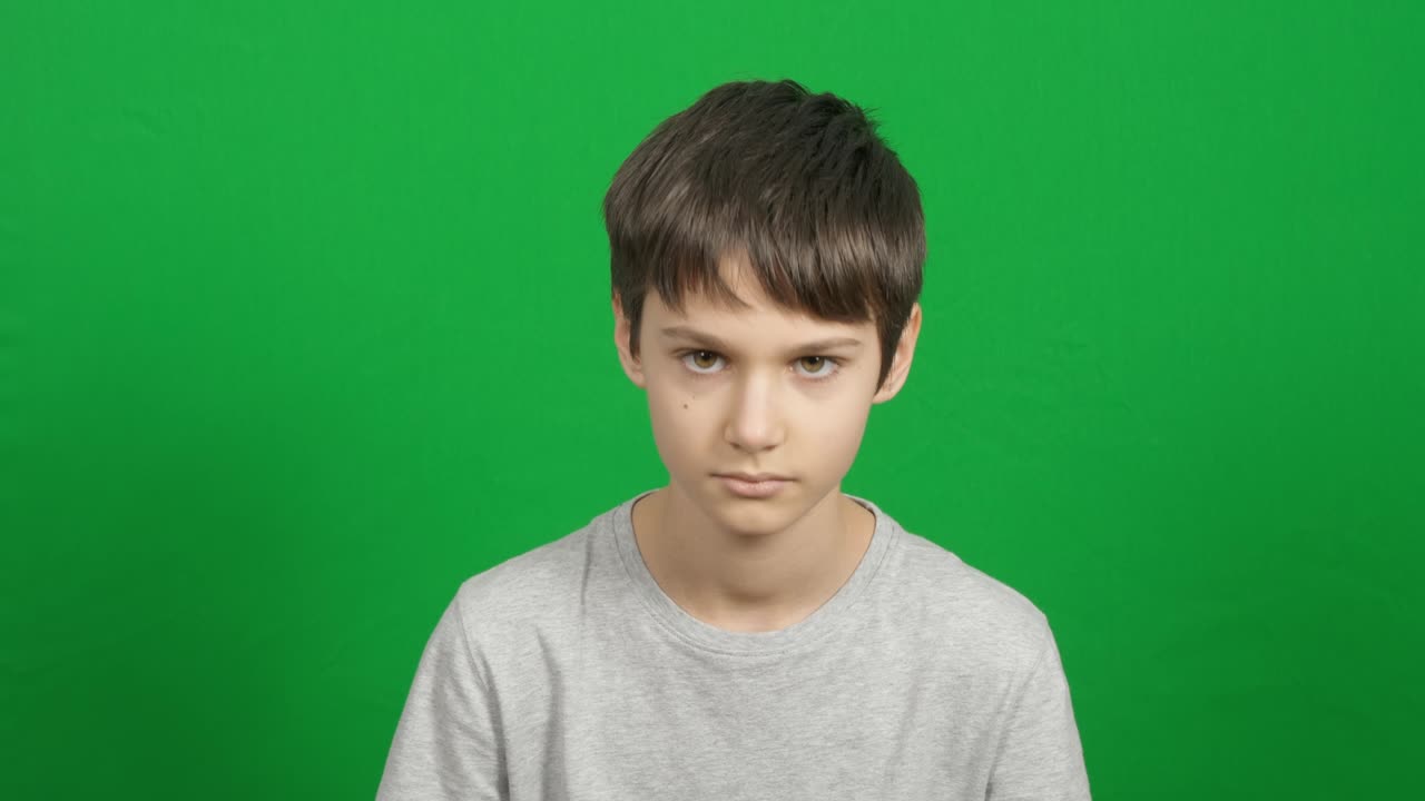 진지하게 생각하고 호기심이있는 십대가 머리를 들어 카메라를 바라보고 있습니다. 평온하고 혼자 불행한 젊은 소년은 녹색 크로마 키 배경에서. 가까운 아이 초상화.