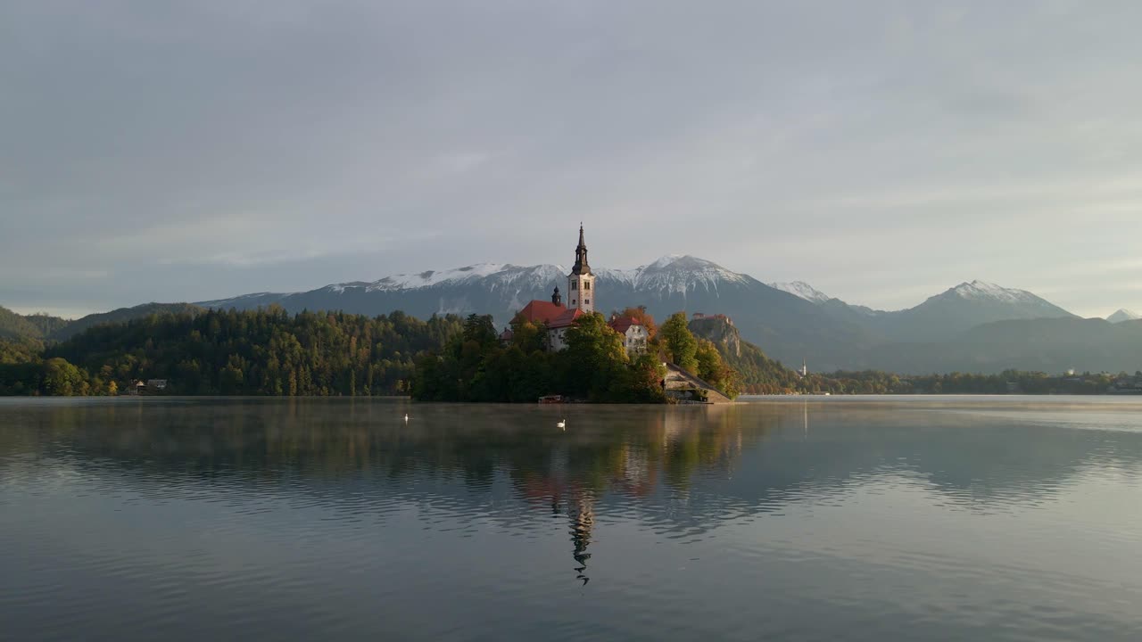 Serena vista mattutina dell'isola del Lago di Bled con chiesa e montagne innevate