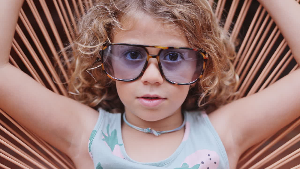 Cool little girl in a garden chair with sunglasses making faces