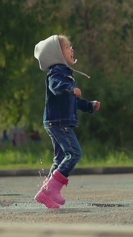 slow motion child happily jump deep puddle rainboots, hood jacket, girl has fun after self-isolation in street, laugh scream, look up sunny weather after rain end of quarantine exit self-isolation