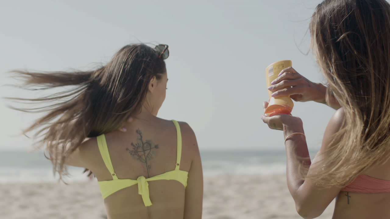 Slow motion of girl applying sunscreen on friends back