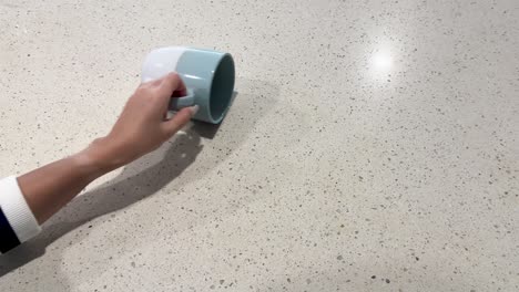 a hand accidentally tips over a mug, spilling coffee onto a kitchen countertop