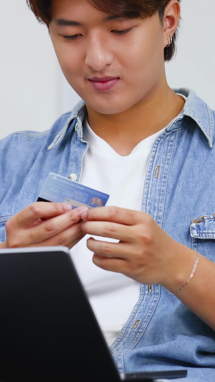 An Asian man enters credit card details into a laptop for an online purchase transaction