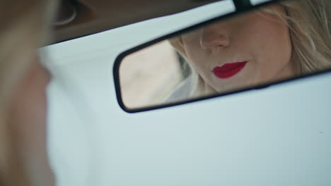 car mirror reflecting beautiful woman applying red lipstick on lips close up.