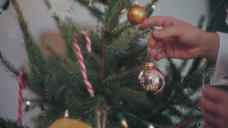 hands decorating christmas tree with silver bauble at home