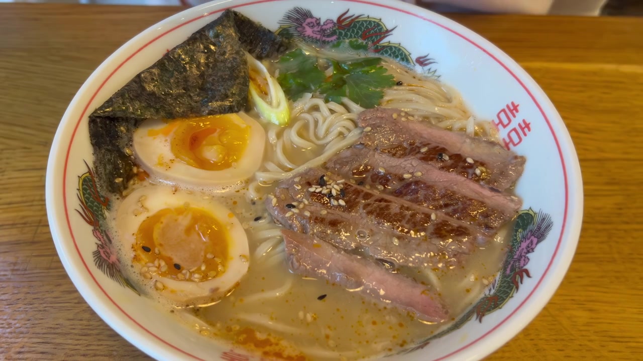 Primo piano di un cucchiaio giapponese che raccoglie ramen tonkotsu fumante con ricco brodo di maiale, fette di maiale chashu, uovo semi-sodo, alga nori e cipollotti verdi.