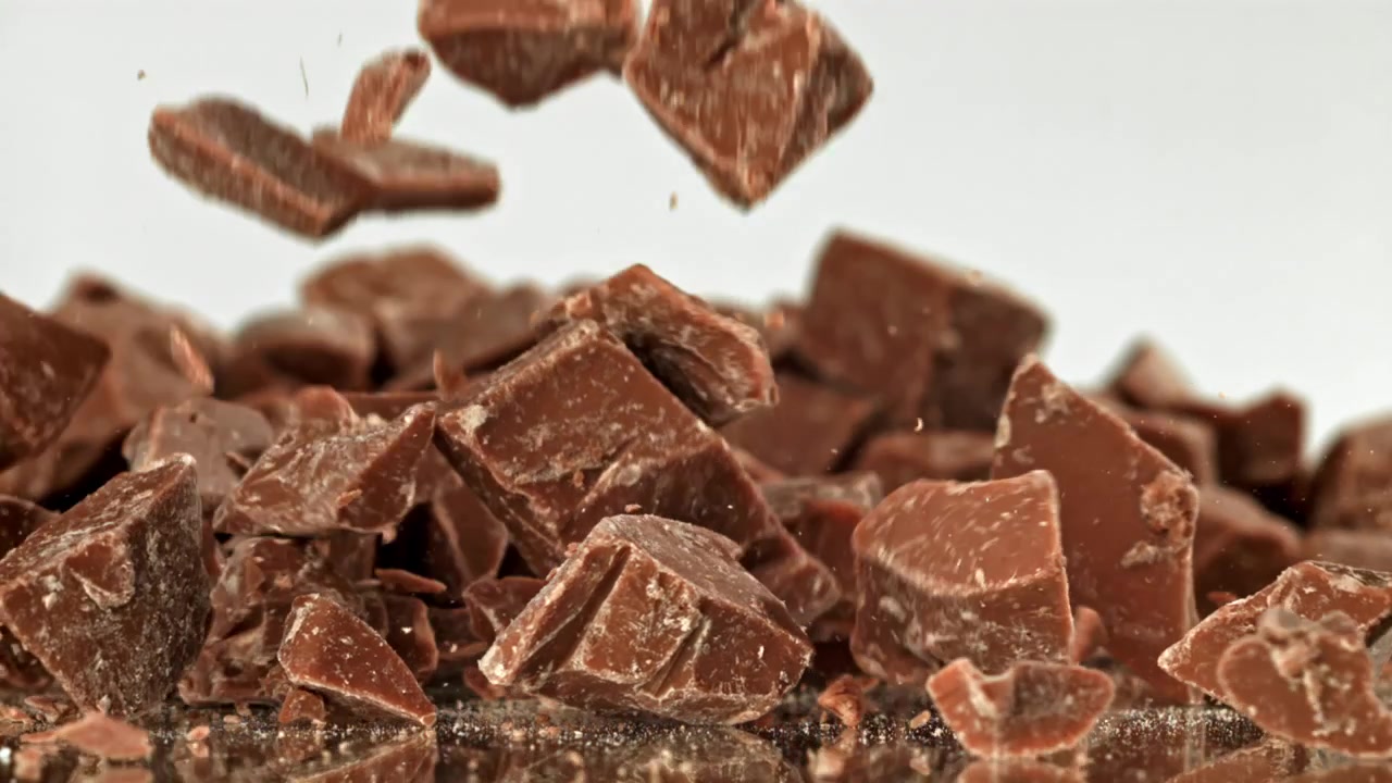 Primo piano di pezzi di cioccolato che cadono su superficie riflettente