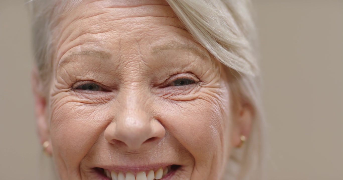 Senior woman, studio, lifting lids and opening eyes, smiling, showing teeth with stud earrings