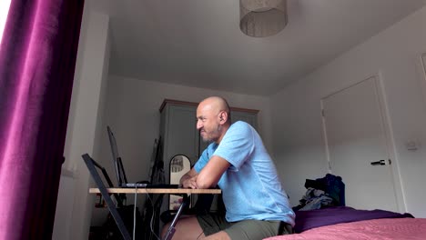 a man sitting in a bedroom working remotely on a laptop at a desk.