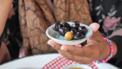 a woman's hand reaches for a black olive from a small plate.