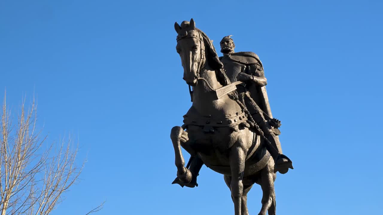 Uma majestosa escultura de bronze do herói nacional Gjergj Kastrioti Skanderbeg a cavalo, dominando a ampla praça de pedestres de pedra no coração do centro metropolitano.