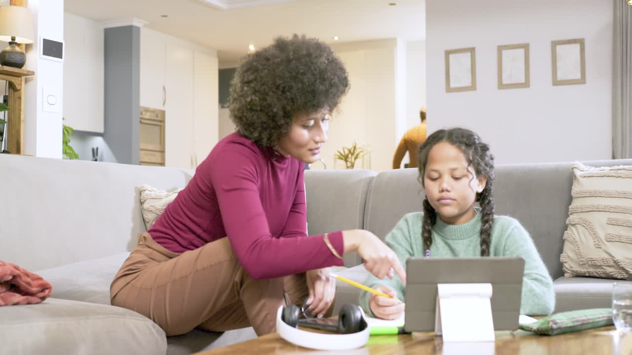 African American family using tablet at home guiding daughter writing while father bringing mugs