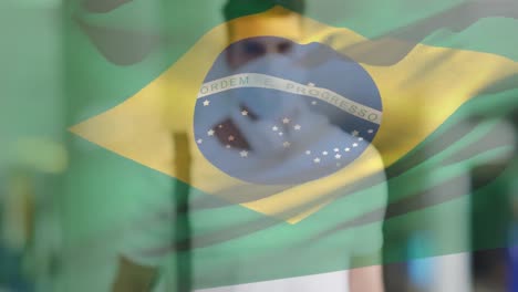 Animation-of-flag-of-brazil-waving-over-latin-man-wearing-face-mask-in-city-street