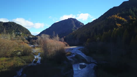 backwards drone dolley shot of water streaming between the autumn colored trees