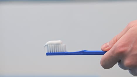 A-woman-in-the-bathroom-squeezes-white-toothpaste-from-a-tube-onto-a-blue-toothbrush-on-a-white-background,-brushing-her-teeth,-morning-and-evening-procedures,-hygiene