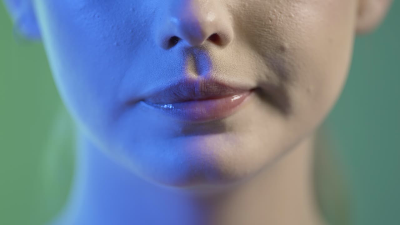 Close Up Of Woman's Face and Mouth, Taking a Bite and Eating Orange Slice, Studio Shot With Colorful Lighting