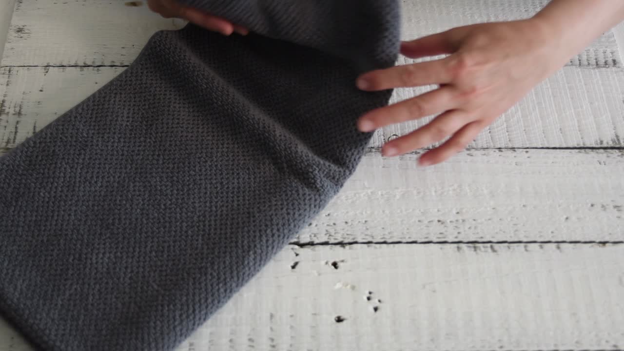 Woman's folding a grey towel to place it on the shelf.