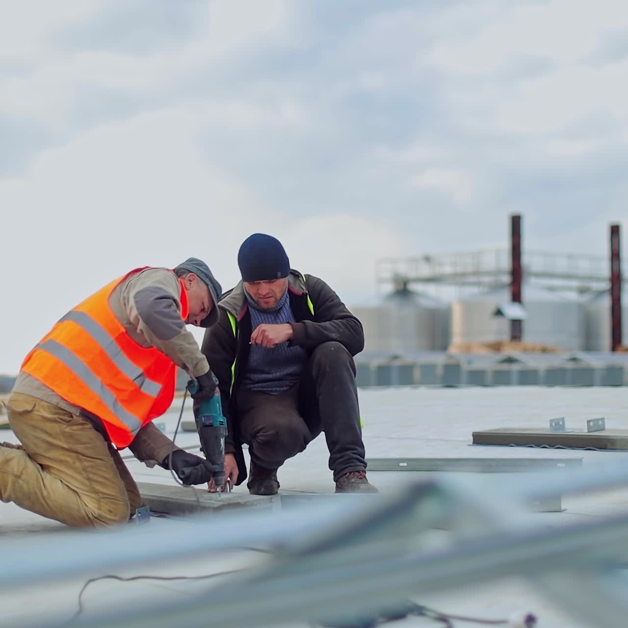 Solar technicians working on a solar farm using a drill. Workers installing photovoltaic solar panels on the roof of building, which converts solar energy into electric energy.