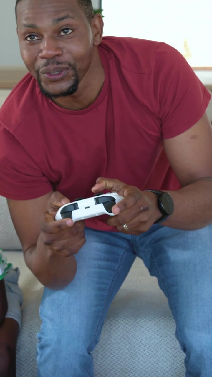 Camera panning showing sitting man grabbing gamepad, leaning and waving for friendly play