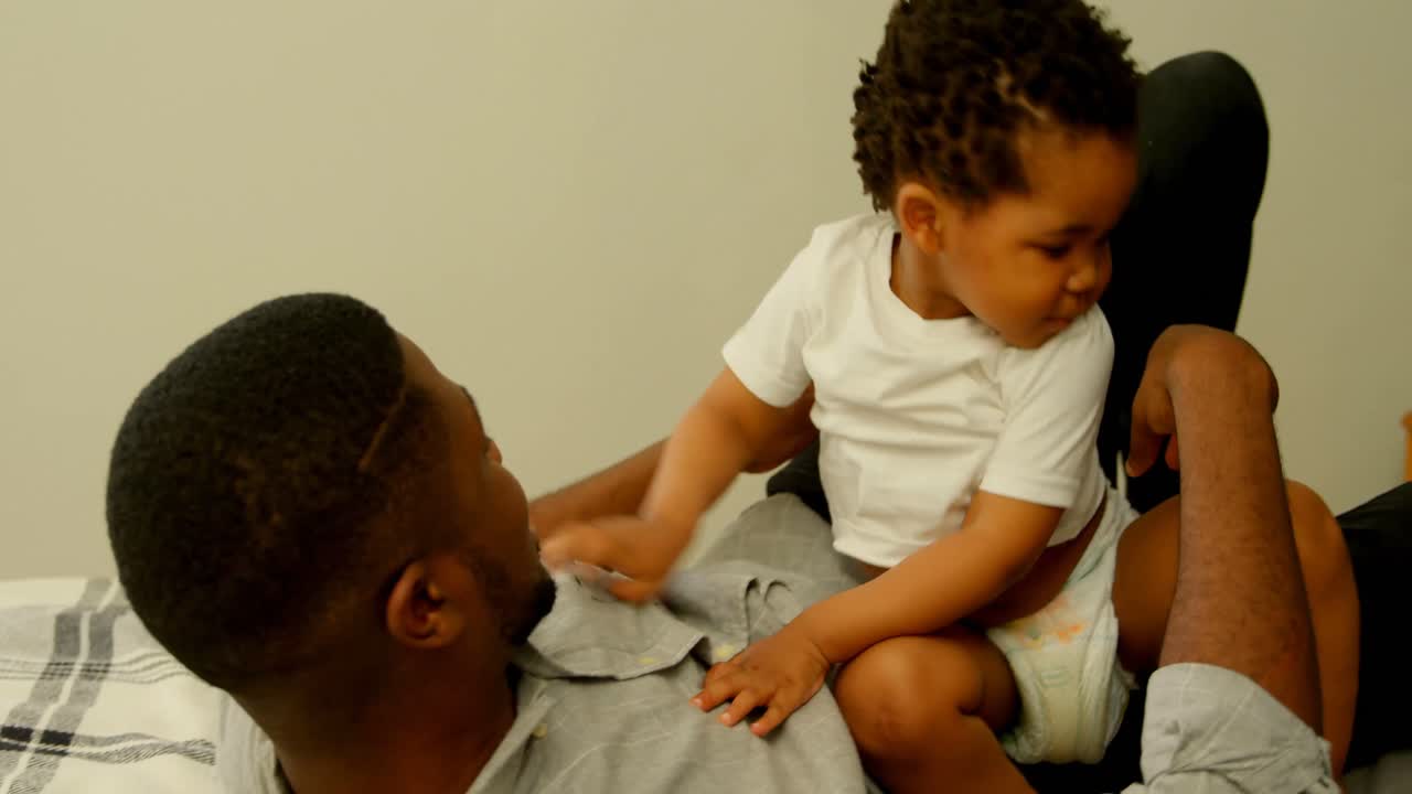 Side view of young black father playing with his son on bed in bedroom of comfortable home 4k